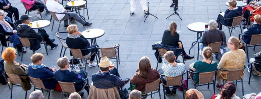 Yleisö istuu ulkona puoliympyrässänja keskellä soittaa kaksi viulistia.