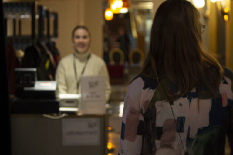 Tummahiuksinen henkilö kuvattuna takaapäin kävelemässä lipunmyyntipisteelle