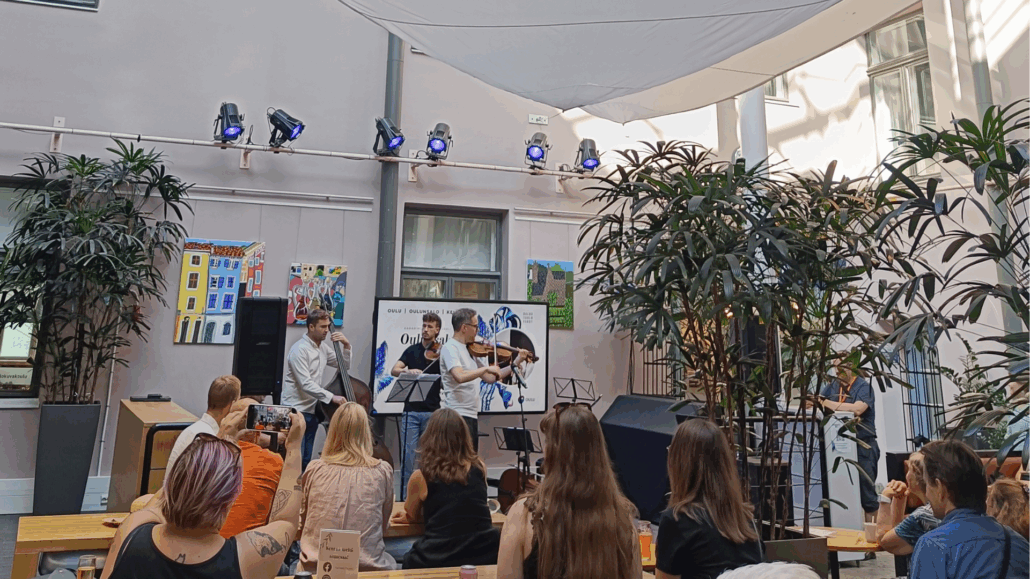 kahvilan lavalla kolme muusikkoa soittaa, etualalla yleisöä