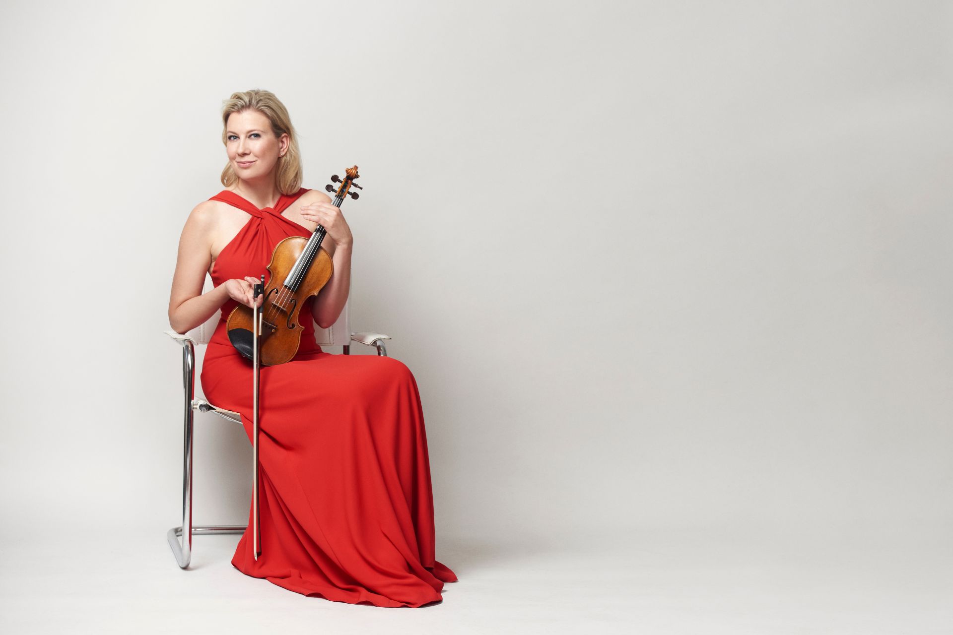 nainen pitkässä punaisessa mekossa istuu tuolilla viulu sylissään