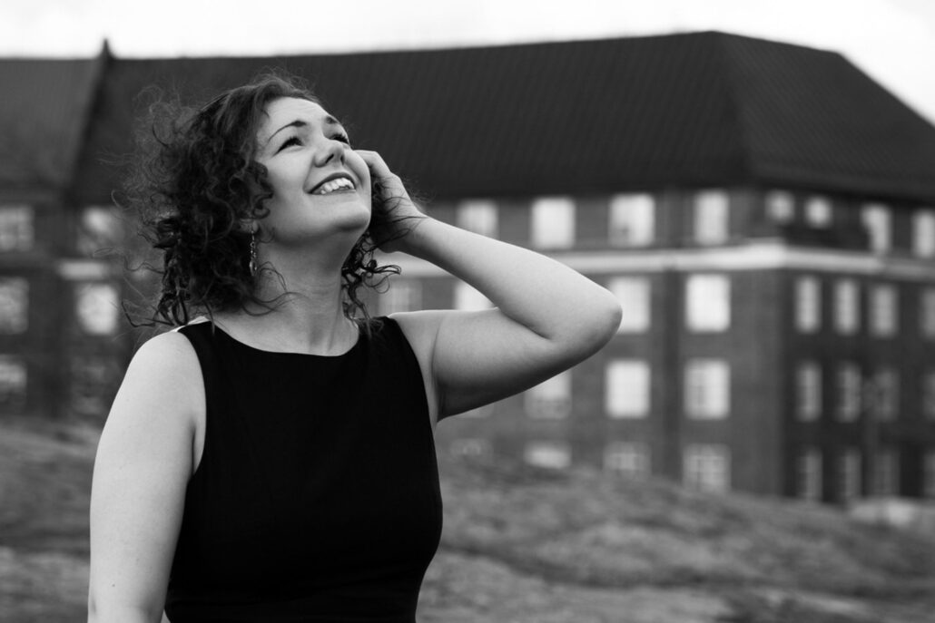 hymyilevä nainen katsoo taivaalle, taustalla kerrostalo