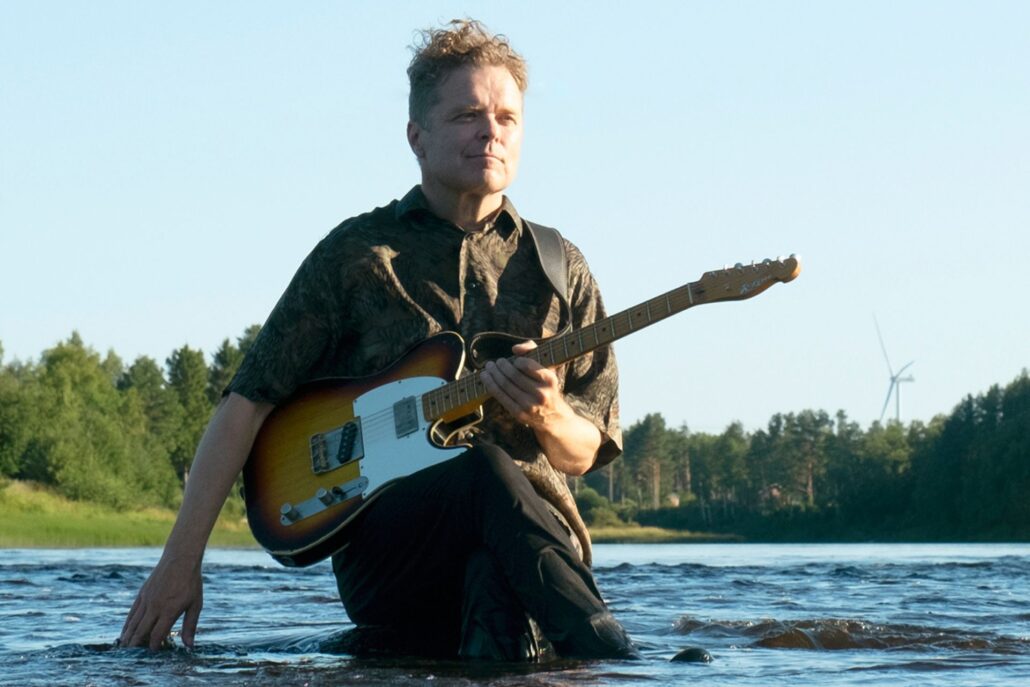 mies istuu joessa ja pitää sähkökitaraa sylissä