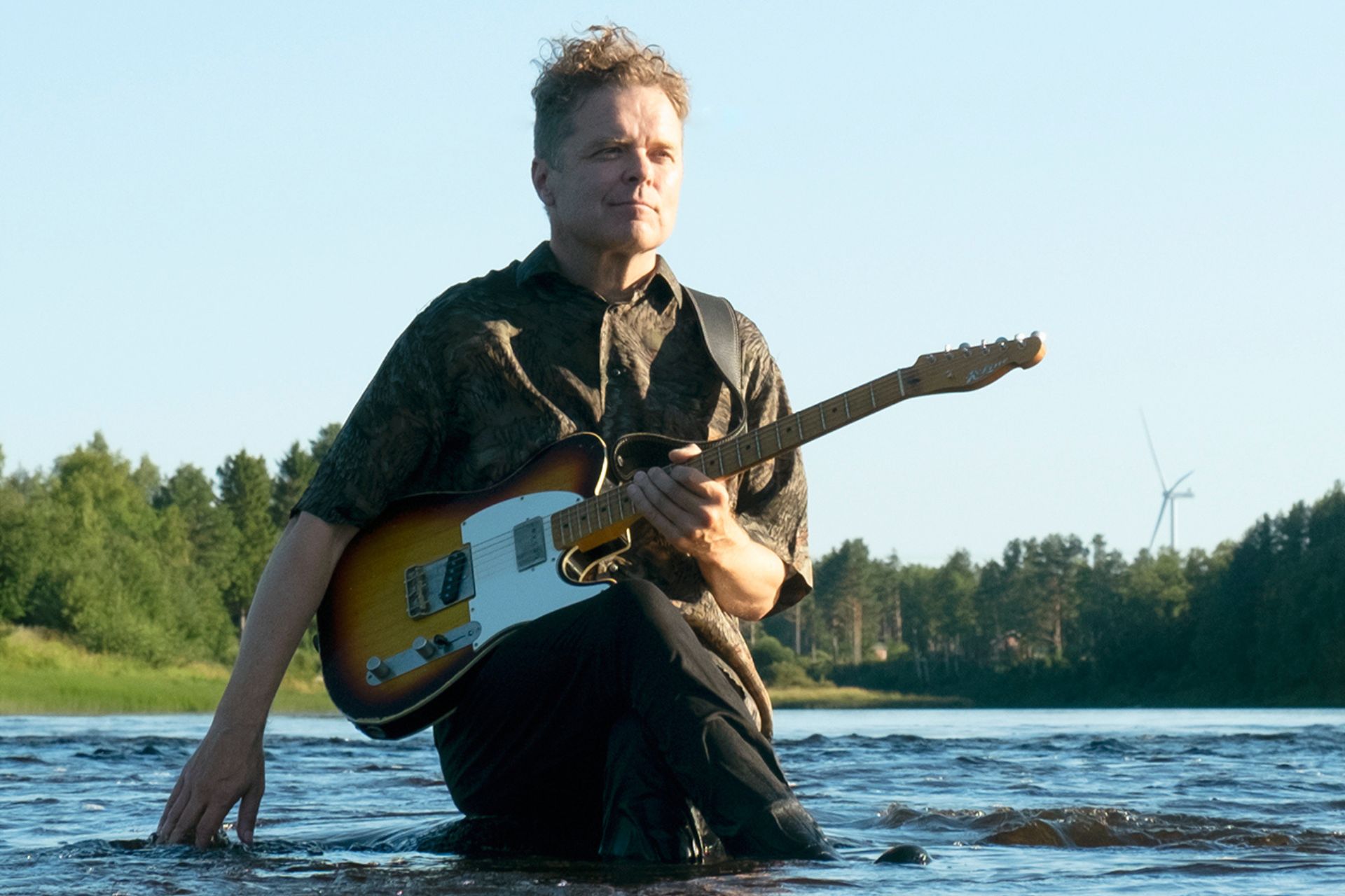 mies istuu joessa ja pitää sähkökitaraa sylissä