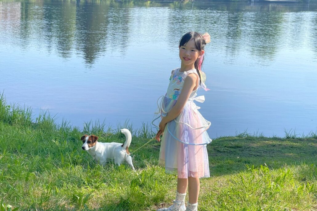 mekkoon pukeutunut tyttö seisoo veden edessä ja pitää koiraa talutushihnassa