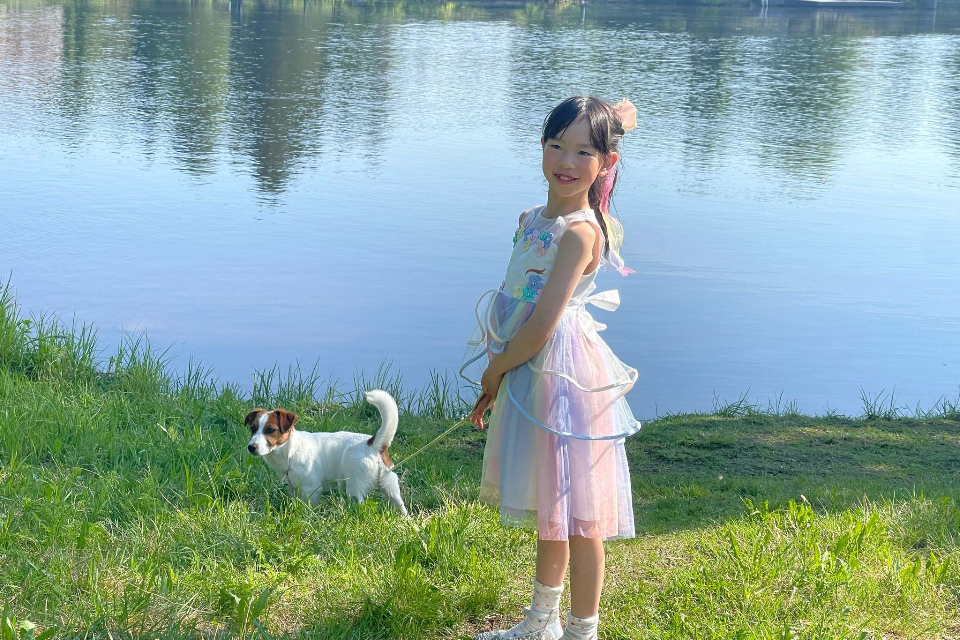 mekkoon pukeutunut tyttö seisoo veden edessä ja pitää koiraa talutushihnassa