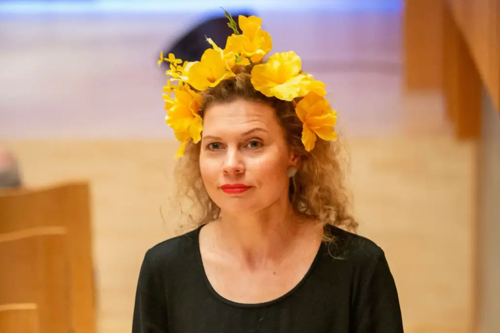 kiharahiuksinen nainen keltainen kukkaseppele päässään, taustalla konserttisali
